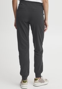 Sorte joggebukser med elastisk midje, tapered fit og avsmalnende ankler. To baklommer, laget av mykt materiale. Kombinert med grå og hvite joggesko.