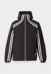 Veste noire avec un col haut, fermeture éclair et poches latérales. Accentuée de rayures crème et d'un petit patch logo sur l'ourlet.
