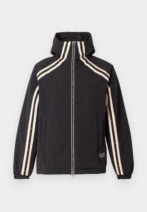 Black jacket featuring a high collar, zip closure, and side pockets. Accented with cream stripes and a small logo patch on the hem.