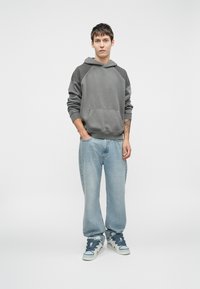 Gray hoodie with a kangaroo pocket and raglan sleeves, paired with light blue straight-leg jeans and patterned high-top sneakers.