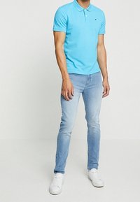 Polo azzurra chiaro con colletto, maniche corte e piccolo logo. Abbinata a jeans azzurri chiari e scarpe da ginnastica bianche.