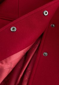 Roter Wollmantel mit glatter Satinfütterung, die mit Ripsbandmustern versehen ist. Silberne Druckknöpfe sichern die vordere Lage und geben einen kontrastierenden Innenraum frei.