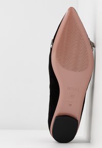 Semelle d'une chaussure plate pointue en daim noir avec une semelle extérieure en caoutchouc couleur fauve, motif à vagues et petit talon bloc, taille 38 estampillée sur la semelle.