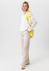 Lichtgewicht witte gebreide cardigan met citroenenprint, gecombineerd met een eenvoudig wit topje en beige broek; model staat met handen in de zakken.
