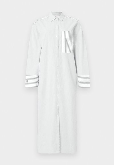 Μακρύ λευκό φόρεμα με κουμπιά και λεπτές κάθετες μαύρες ρίγες, ριγέ τσέπη στο στήθος και φαρδιές ριγέ μανσέτες στα μακριά μανίκια.