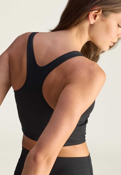 Czarny sportowy top crop z plecakiem, o dopasowanym kroju, wykonany z gładkiego, elastycznego materiału z minimalną ilością szwów.