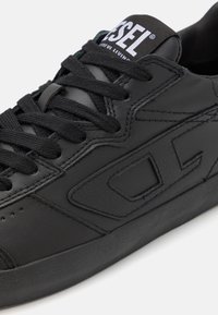 Sneaker in pelle nera con superficie texturizzata, punta tonda e lacci neri. Presenta un logo sulla linguetta e dettagli geometrici sui lati.