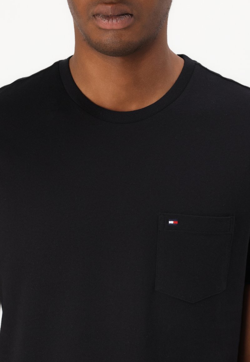 Czarna bawełniana koszulka z okrągłym dekoltem, wyposażona w małą kieszonkę na piersi oraz logo marki w kolorach czerwonym, białym i niebieskim. Miękka w dotyku.