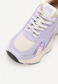 Sneaker viola e beige con tomaia in rete, dettagli testurizzati e lacci bianchi. Presenta un colletto imbottito e suola in gomma.