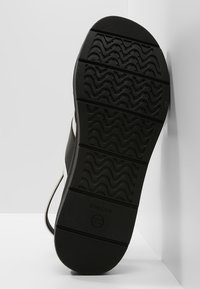 Musta kumipohja, jossa on aaltoileva tekstuuri, sileä reuna ja brändin 'GEOX' logo sivussa.