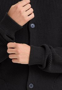 Cardigan nero a coste con chiusura a bottoni e polsini risvoltati, che presenta una superficie testurizzata e una vestibilità rilassata.