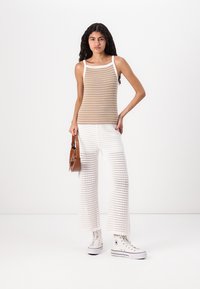 Brun og hvit stripete tank topp, parret med hvite heklede vide bukser. Hvite høyhælte sneakers og en brun skulderveske fullfører antrekket.