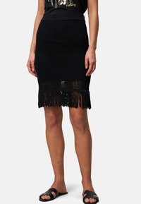 Jupe noire en tricot avec une taille ajustée et un détail de franges à l'ourlet, fabriquée à partir d'un matériau léger. Assortie à des sandales plates noires.