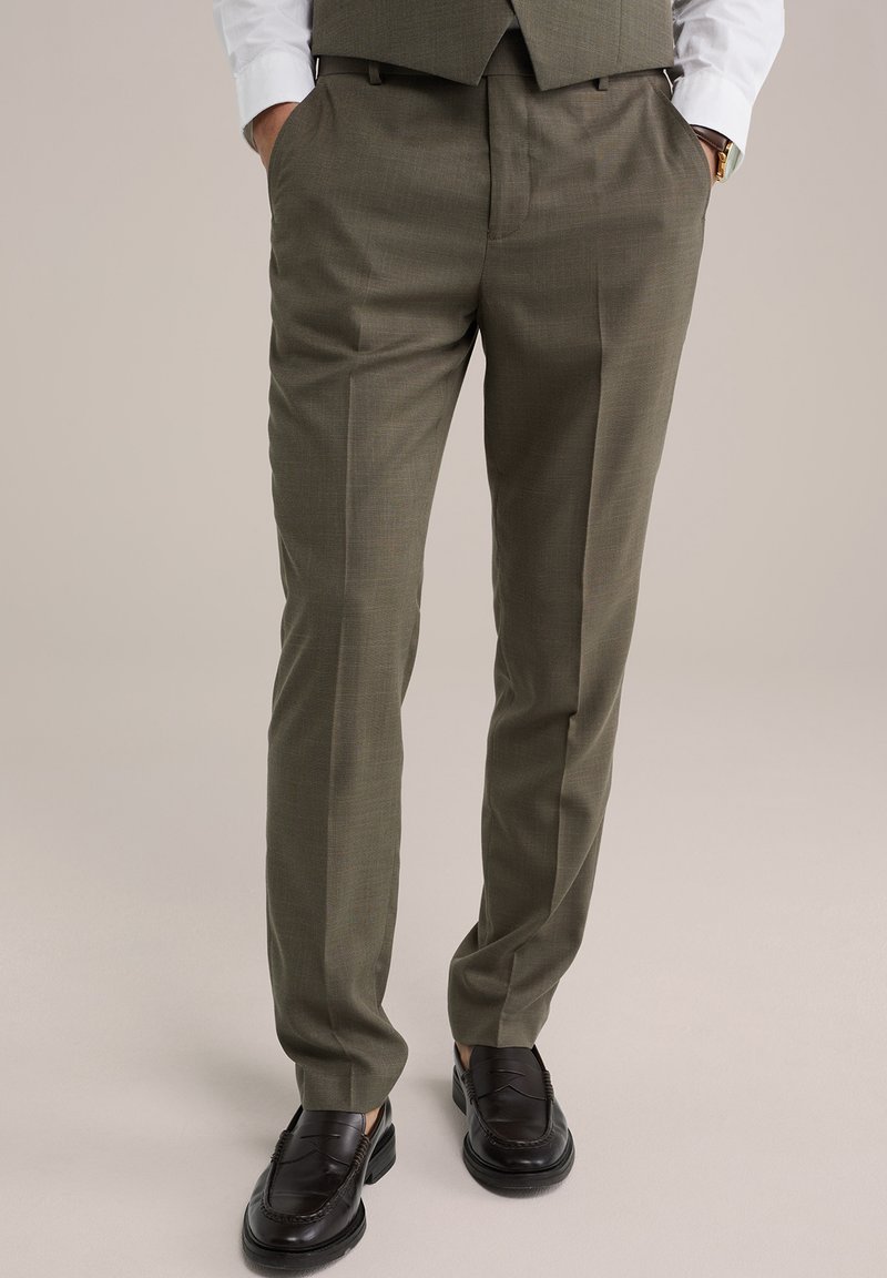 Oliva zöld nadrágok texturált felülettel és sima elülső résszel, oldalsó zsebekkel és szűkített szabással. Fekete cipővel viselve.