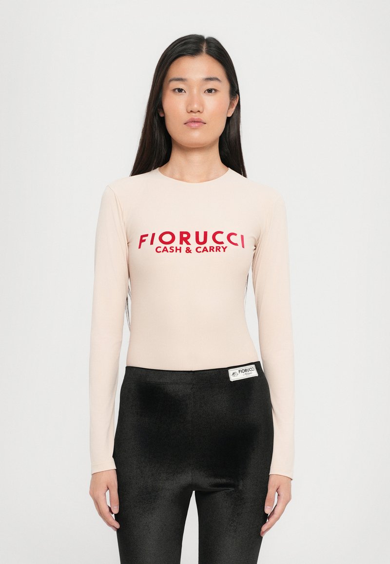 Bodysuit s dugim rukavima u nijansi kože s crvenim logotipom "Fiorucci Cash & Carry"; upareno s crnim sjajnim tajicama, stvarajući elegantnu siluetu.