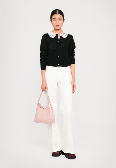 Black knitted cardigan with a white lace collar, paired with white flared pants and a light pink handbag, featuring flat shoes with a glossy finish.