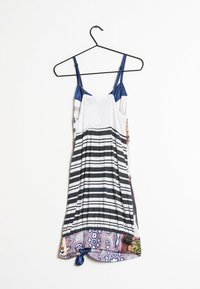 Abito senza maniche con top in satin blu, busto bianco strutturato e gonna a strisce bianco e nero con un orlo decorato da un motivo colorato.