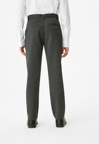 Pantalons gris ajustés avec une texture lisse, à jambe droite, et une poche arrière avec un bouton. Associés à une chemise blanche à manches longues.