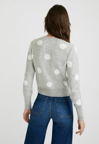 Pull gris à gros pois blancs, avec des poignets et un ourlet côtelés, associé à un jean bleu taille haute. Matière en mélange de laine douce.