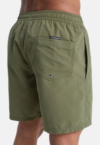 Shorts de bain vert olive en tissu lisse et léger ; dotés d'une taille élastique, de poches latérales et d'une poche arrière avec un œillet en métal.