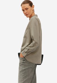 Lichtgrijze langemouwen shirt met een borstzak en knoopmansjet, gecombineerd met grijze jeans. Soepele stof en een relaxte pasvorm. Eenvoudig ontwerp.