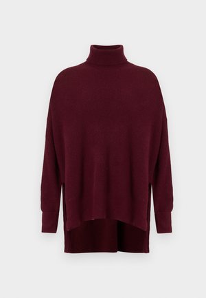 Pull col roulé surdimensionné bordeaux avec manches longues et fentes latérales, présentant un ourlet asymétrique.