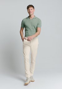 Groen polo met korte mouwen, beige getailleerde broek en lichtgekleurde sneakers. Eenvoudig ontwerp met een klassieke kraag en minimale details.