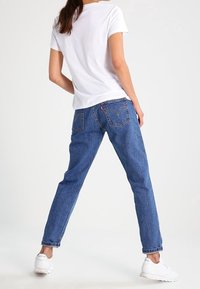 Camiseta blanca liviana de manga corta, combinada con jeans de mezclilla azul medio de corte relajado y bolsillos traseros distintivos.