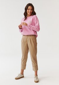 Roze sweatshirt met ronde hals met de tekst "MY FOREVER COAT"; beige cropped broek; lichtgekleurde sneakers. Casual fit, zacht stof, ontspannen stijl.