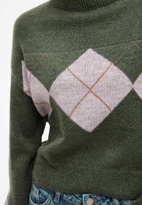 Pull en tricot vert avec un grand motif argyle rose clair et marron, porté avec un jean en denim bleu.