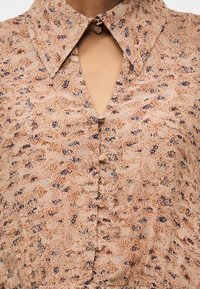 Μπεζ μπλούζα με αφηρημένο καφετί και μπλε πουά μοτίβο, με μυτερό γιακά και κουμπιά καλυμμένα με ύφασμα.