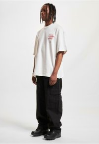 Bílý oversized tričko s červenými tištěnými detaily, spárované s černými cargo kalhotami a černými botami. Jednoduchý design, měkká tkanina, uvolněný střih.