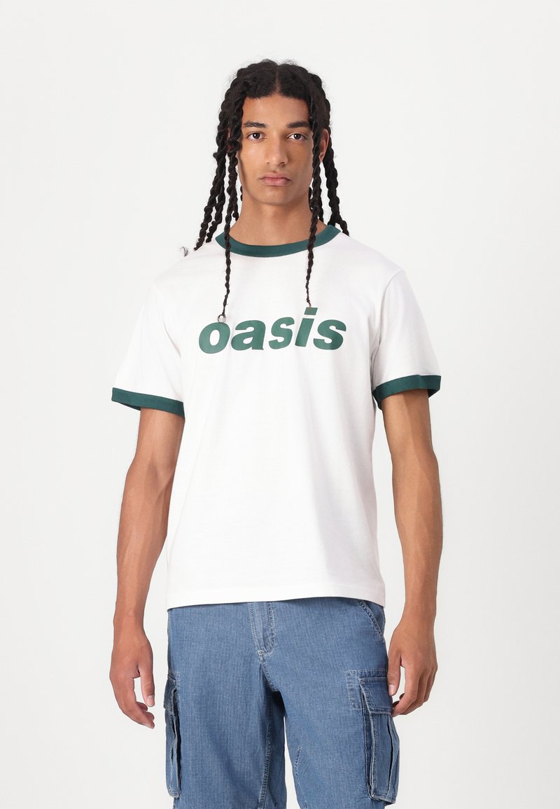 White cotton t-shirt with green ribbed collar and sleeves, featuring bold green "oasis" text on the front, worn with blue cargo shorts.