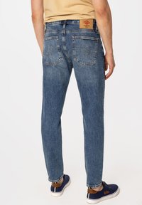 Jasnoniebieskie dżinsy z prostą nogawką, z dwoma tylnymi kieszeniami oraz prostokątną naszywką z logo na pasku od spodni.