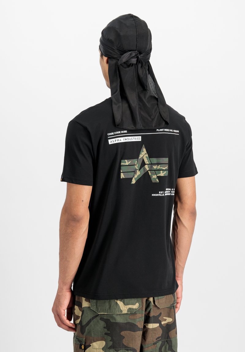 T-shirt noir à manches courtes avec un graphisme camouflage au dos, comportant des détails textuels. Porté avec un durag en satin noir. Pantalons camouflage.