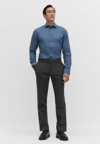 Niebieska koszula z guzikami o gładkiej fakturze, w połączeniu z dopasowanymi ciemnoszarymi spodniami. Buty są czarne, wypolerowane skórzane.