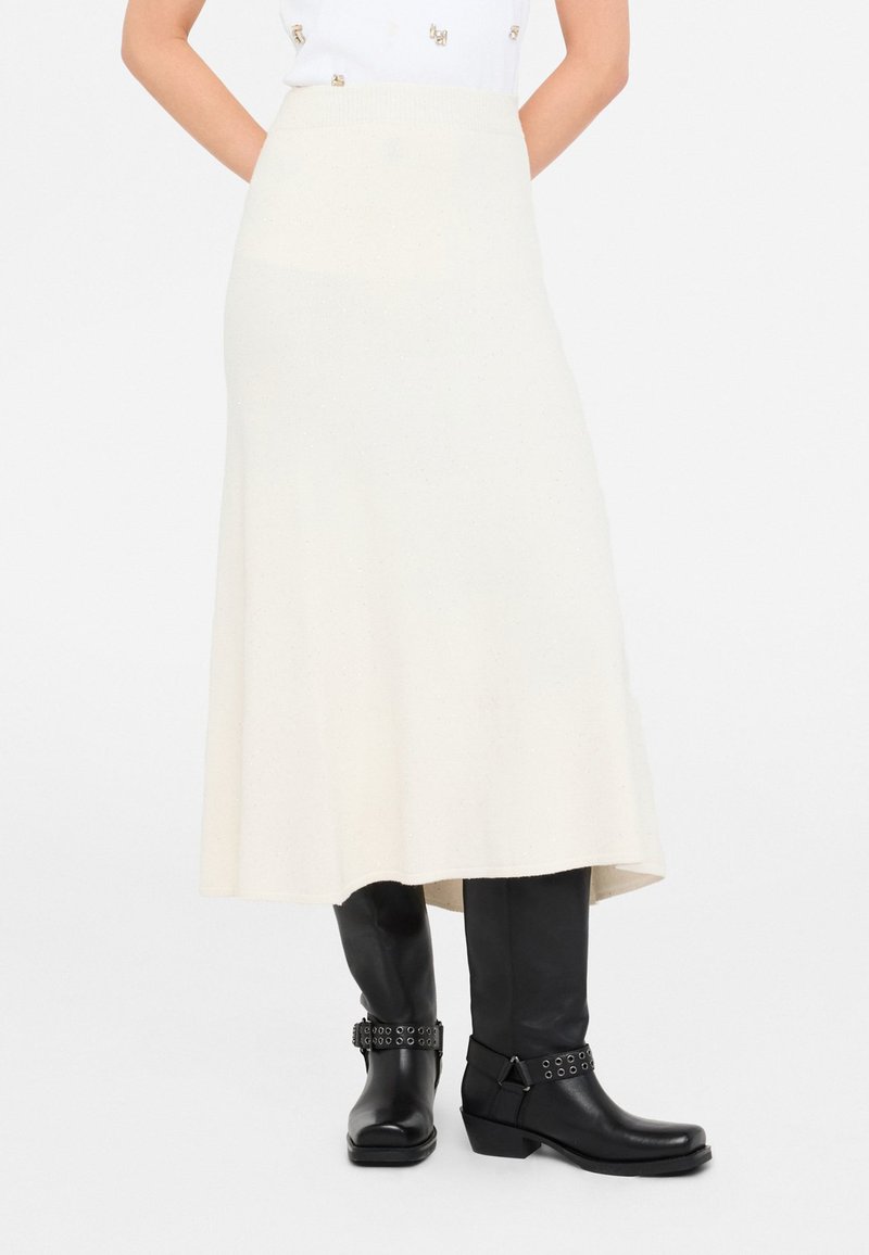 Falda midi de punto en crema con dobladillo acampanado y cintura acanalada, combinada con botas negras hasta la rodilla con acentos de tachuelas.