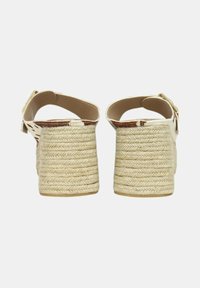 Cuñas de esparto beige con tacón de yute trenzado y correa con hebilla, que presentan un interior liso de un tono marrón claro y un acabado exterior texturizado.