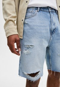 Vaaleansininen farkkushortti, jossa on rispaantuneet reunat, kulutetut repeämät ja rento istuvuus. Ominaisuuksina viisi taskua ja näkyvät ompelukorostukset.