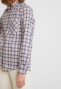 Ljus rutig skjorta i mjukt tyg med rosa, blå och vita rutor, knappade krage, bröstficka och knappade ärmslut.