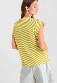 Gestreepte geel-groene top met korte mouwen, losse pasvorm en ronde halslijn, gecombineerd met zilveren shorts. Textuurstof en casual ontwerp.