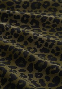 Alyvmedžio žalia medžiaga su juodu leopardų raštu, turinti skirtingų formų ir tekstūrų, demonstruojanti drapavimą ir švelnumą.