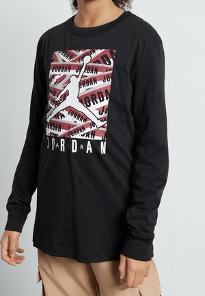 Musta pitkähihainen t-paita, jossa on valkoinen Jordan-logo punamustalla graafisella kuviolla. Pehmeää puuvillakangasta ja rento istuvuus.