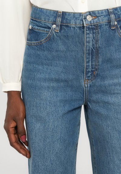 High-waisted blue denim jeans with orange stitching, front pockets, and a button closure. Material appears lightweight and textured.