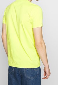 Camiseta de algodón amarilla neón con mangas cortas, escote redondo y dobladillo recto. Presenta una textura suave y un diseño sencillo.