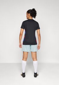 Black short-sleeve sports jersey with colorful side stripes, paired with light blue shorts and white socks, worn with black soccer cleats.