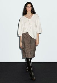Cream oversized sweater, suede brown skirt, and knee-high black boots. Model stands against a plain background, showcasing layered textures.