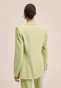 Blazer structuré vert clair avec revers pointus, manches longues et poignets boutonnés. Tissu lisse avec une coupe ajustée et une fente au dos.