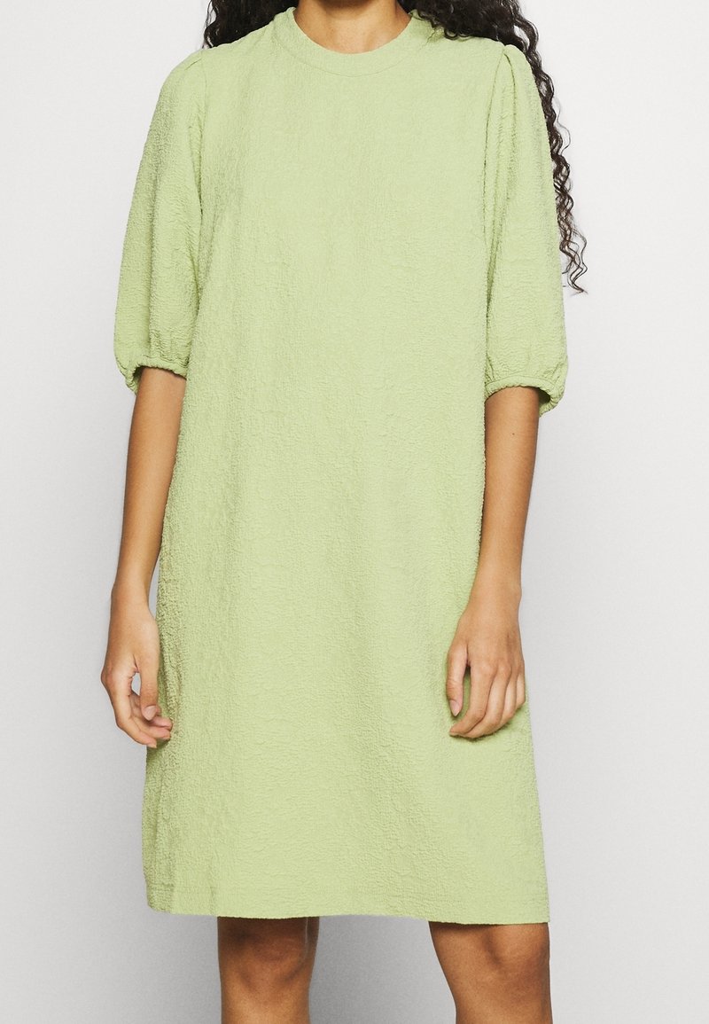 Robe texturée vert clair avec une coupe décontractée, un col rond et des manches courtes bouffantes. Le matériau semble doux et légèrement froissé.