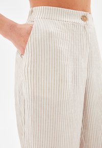 Cotton blend trousers with vertical beige and white stripes, featuring a mid-rise waistband, a single button closure, and side pockets.
